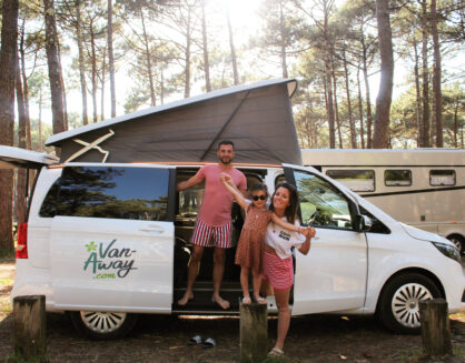Trois personnes devant un van Van Away blanc, porte latérale ouverte et toit relevable déployé, dans un cadre boisé